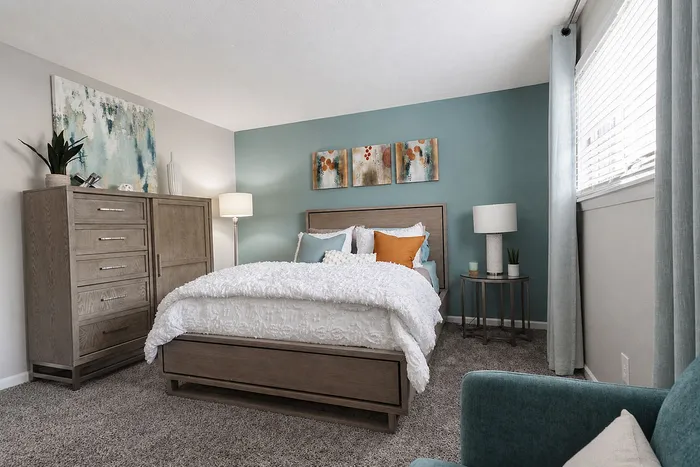 Inviting bedroom with elegant decor, featuring a cozy bed with stylish pillows, warm lighting, and chic artwork on a soothing teal accent wall.