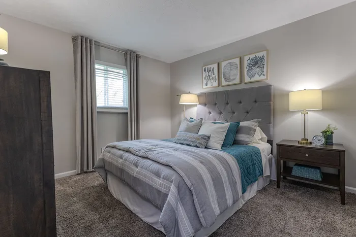 Cozy bedroom with soft grey tones, plush carpet, and elegant decor featuring a tufted headboard and stylish bedside lamps.