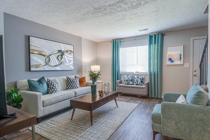 Bright and inviting living room with modern decor, featuring a cozy sofa, vibrant cushions, and stylish artwork, complemented by natural light from a large window with teal curtains.