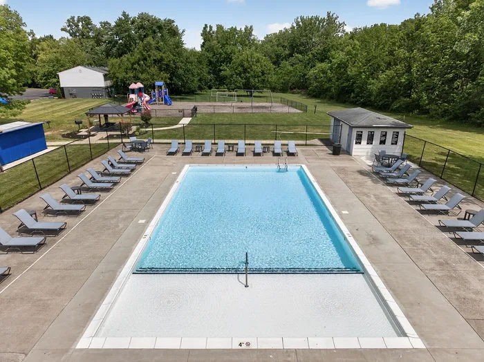 Inviting outdoor pool with surrounding lounge chairs and adjacent playground, set in a lush green environment.