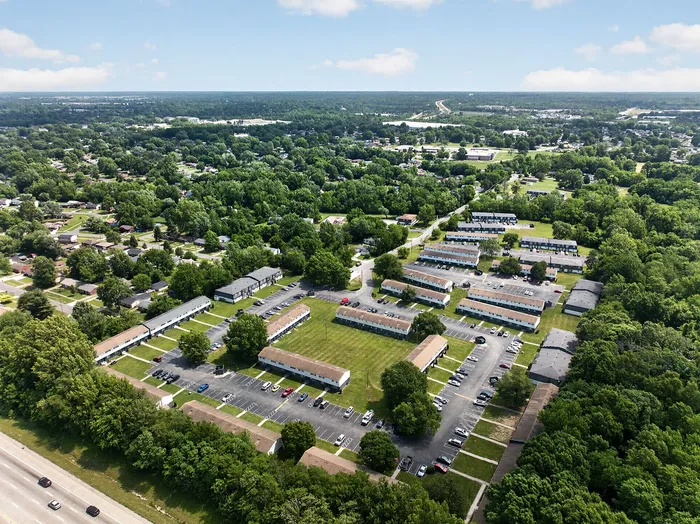 Aerial view of a charming residential community nestled among lush greenery, showcasing neatly arranged apartment buildings and ample parking spaces.