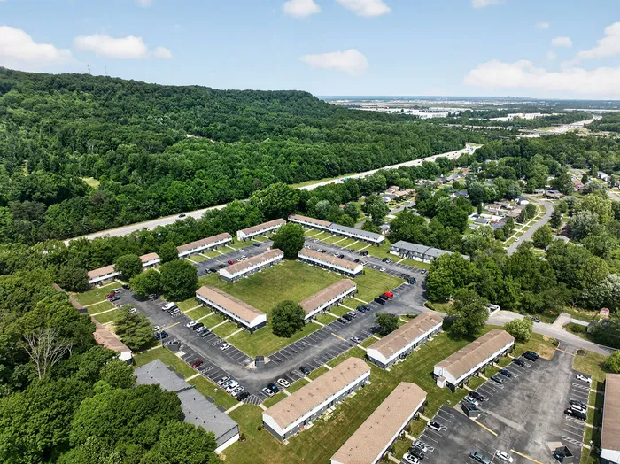 Aerial view of a scenic apartment complex surrounded by lush greenery, offering a serene living environment with easy access to nearby roads.
