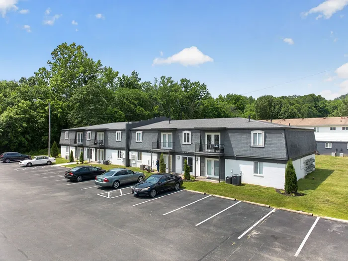 Charming apartment complex with modern design, set amidst lush greenery, featuring ample parking and inviting balconies.