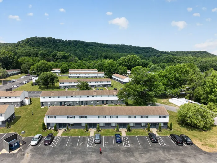 Scenic aerial view of charming apartment complex nestled against lush green hills, offering serene living in a beautifully landscaped community.