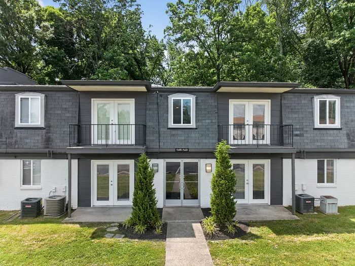 Charming townhouse exterior with modern grey siding, inviting balconies, and lush green landscaping.