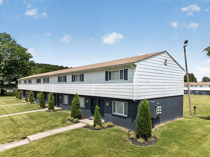Charming townhouse complex with manicured lawns and lush greenery, set against a serene backdrop of rolling hills and clear blue skies.
