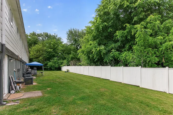 Inviting backyard space with lush green grass, a white privacy fence, and mature trees providing natural serenity and shade.