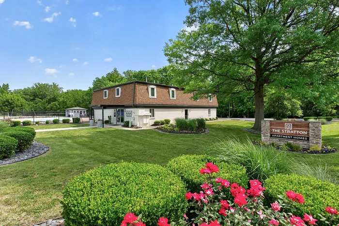 Charming apartment complex surrounded by lush greenery and vibrant flowers, featuring The Stratton sign and inviting outdoor spaces.