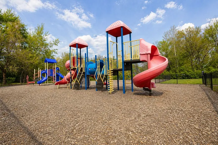 Vibrant playground with colorful slides and climbing structures, surrounded by lush greenery.