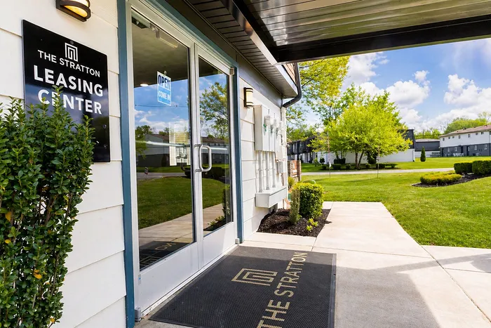 Inviting entrance to The Stratton Leasing Center with lush greenery and modern architecture, promising a welcoming community environment.