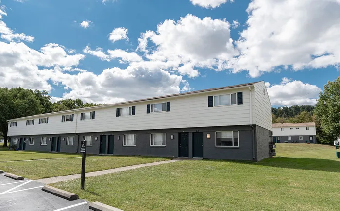 Charming apartment complex with two-story units, surrounded by lush greenery and a clear blue sky.