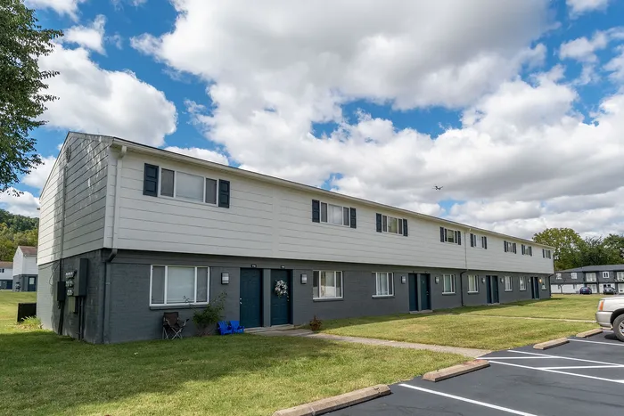 Charming two-story apartment building with modern features, surrounded by lush green lawns under a vibrant blue sky.