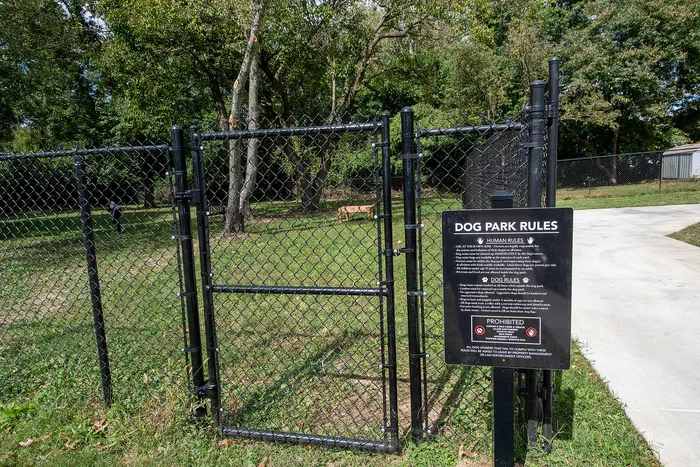 Inviting dog park entrance with clear rules, surrounded by lush greenery and spacious play area, perfect for pets to enjoy.