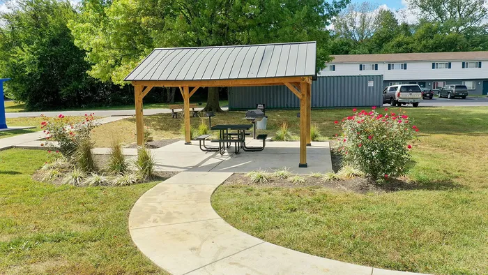 Charming outdoor area featuring a gazebo with picnic tables and grill, surrounded by lush greenery and vibrant flower beds.