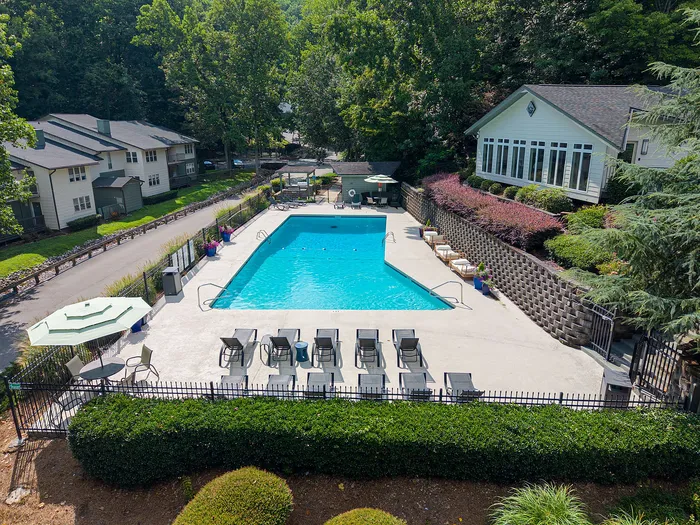 Inviting outdoor pool area surrounded by lush greenery and modern lounge chairs, offering a serene relaxation spot for residents.