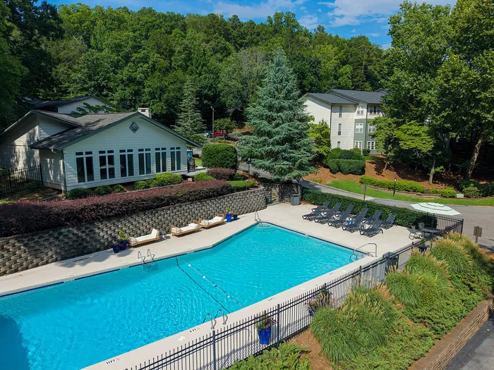 Inviting outdoor swimming pool with sun loungers surrounded by lush greenery and charming residential buildings.
