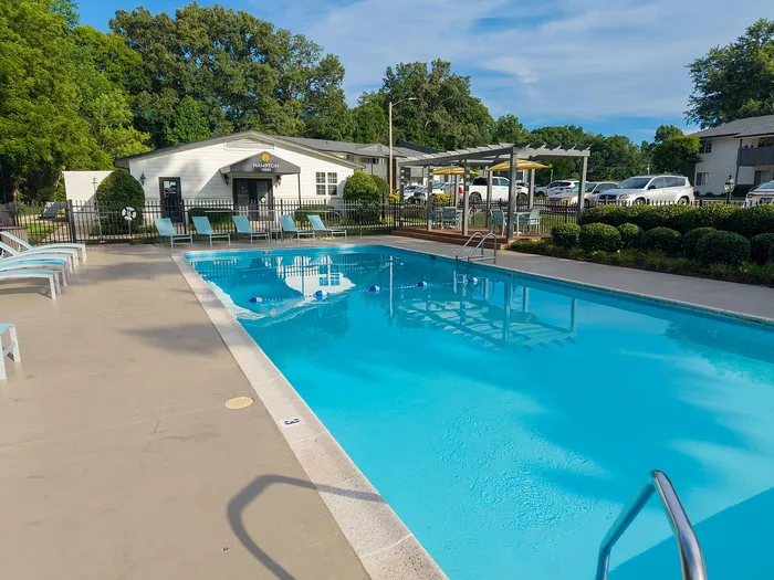 Inviting apartment community pool with lounge chairs and a shaded seating area, surrounded by lush greenery.