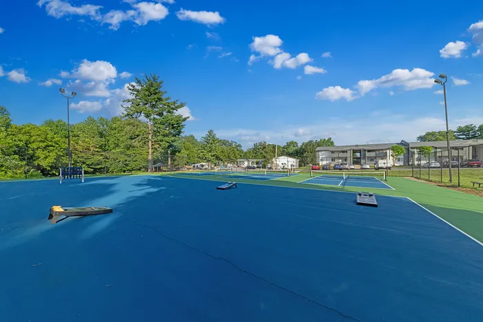 Inviting outdoor sports area featuring multiple tennis courts under a bright blue sky, surrounded by lush greenery and modern apartments.
