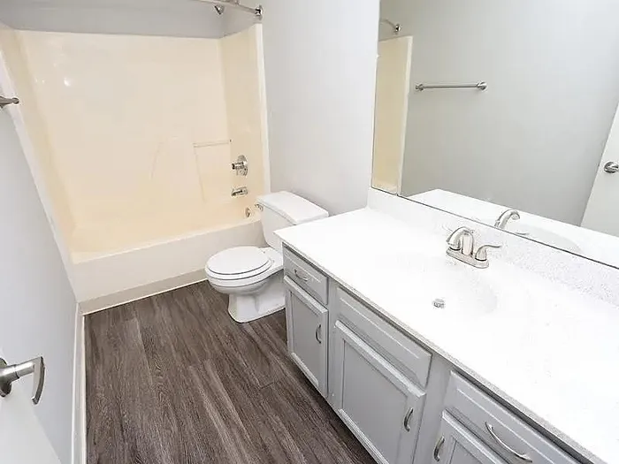Modern bathroom featuring elegant vanity, sleek white countertops, and a spacious tub with warm wood flooring.