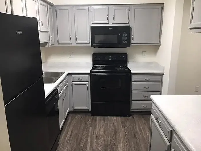 Modern kitchen with sleek gray cabinetry, black appliances, and elegant wood flooring.