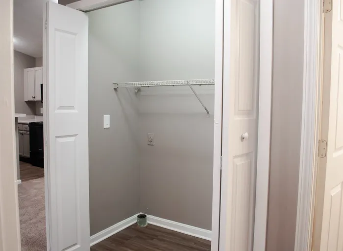 Spacious apartment closet with modern gray walls, sleek shelving, and a glimpse of adjacent kitchen area.