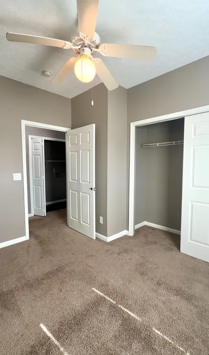 Bright bedroom with plush carpeting, modern ceiling fan, and spacious closet in a stylish apartment.