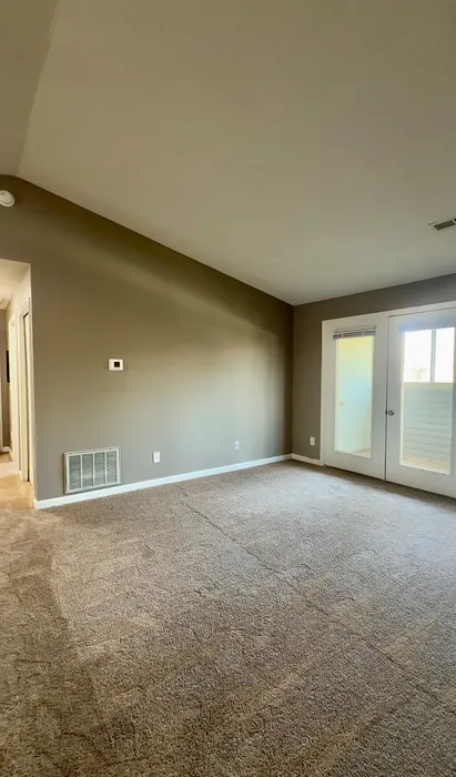Bright and airy room featuring plush carpet and a large window with French doors leading to a charming balcony.