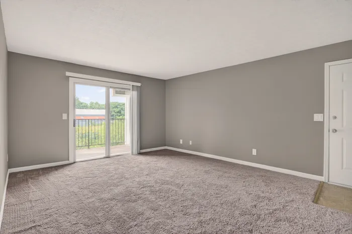 Bright and spacious living room with plush carpet, large sliding glass doors, and a scenic balcony view.
