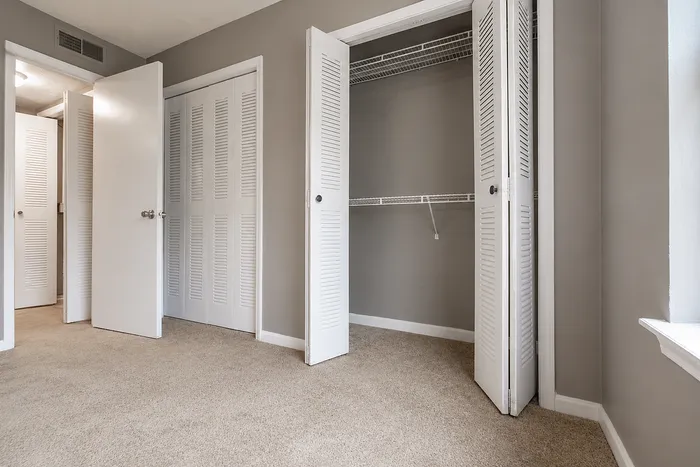 Bright bedroom featuring plush carpet and spacious closets with white louvered doors.