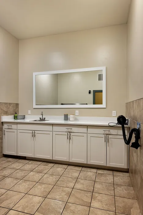 Modern laundry room featuring sleek cabinetry, large mirror, and tile flooring with convenient sink and wall-mounted hairdryer.