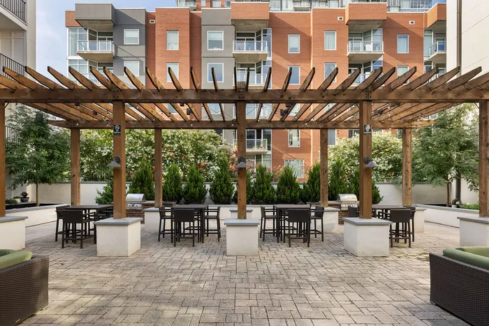 Chic urban courtyard featuring a pergola with modern seating, surrounded by lush greenery and contemporary architecture.