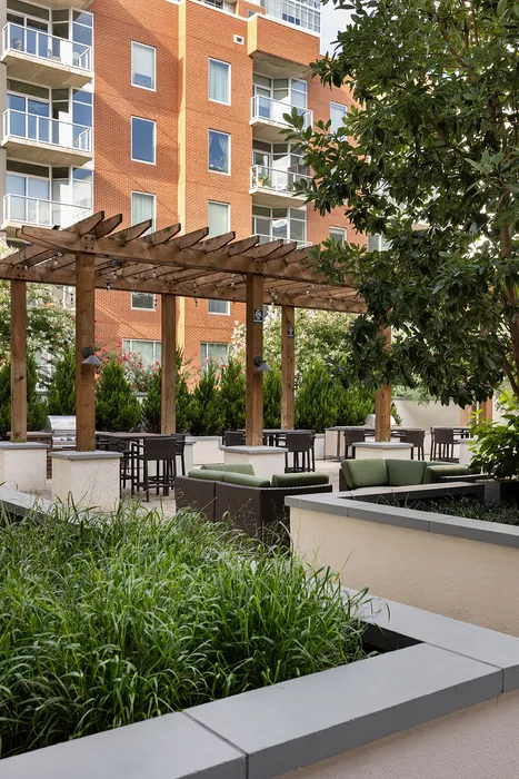 Elegant outdoor patio area with comfortable seating, lush greenery, and wooden pergola, perfect for relaxation and entertaining.