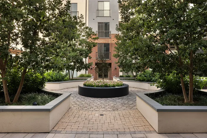 Charming garden courtyard featuring lush greenery, elegant pathways, and a central flower bed at a modern apartment building.