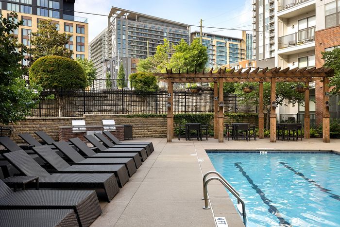 Luxurious urban apartment complex with a stylish outdoor pool area, surrounded by lounge chairs and a charming wooden pergola, perfect for relaxation and entertaining.