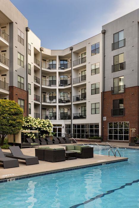 Luxurious apartment complex with a sparkling pool, stylish lounge chairs, and lush landscaping, perfect for relaxation and leisure.