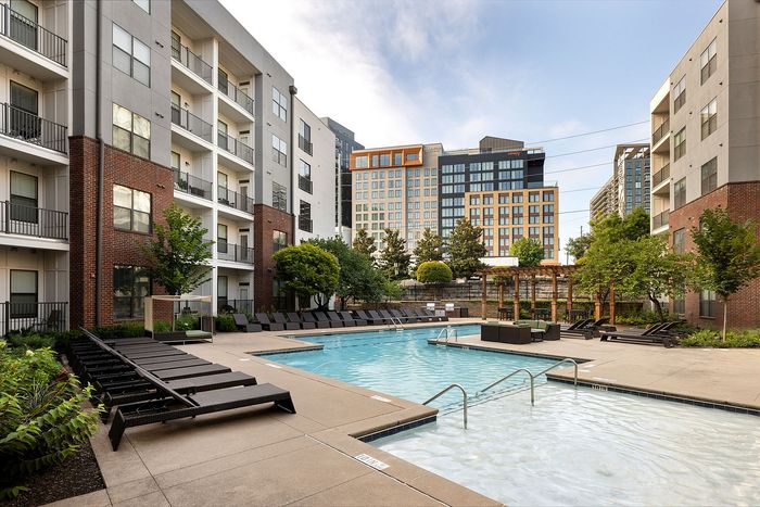 Contemporary apartment complex featuring a luxurious outdoor swimming pool with stylish loungers and lush landscaping, perfect for relaxation.