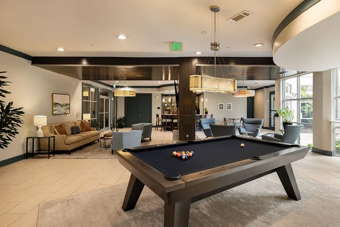 Chic apartment lounge with a pool table, cozy seating area, and stylish modern decor illuminated by elegant lighting.