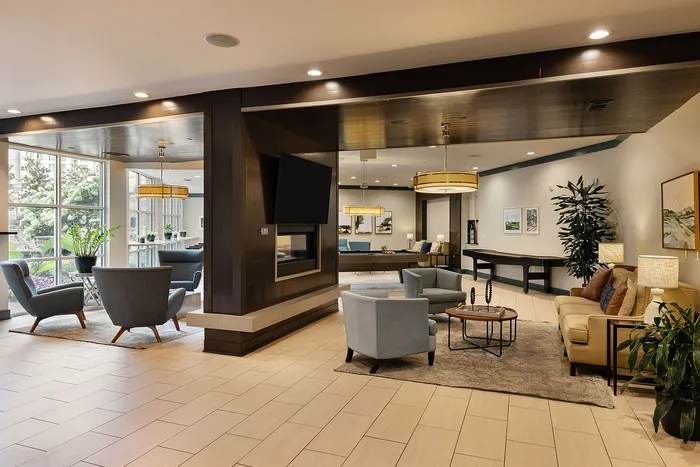 Elegant and inviting apartment lobby featuring modern seating areas with plush chairs, a stylish coffee table, and large windows offering abundant natural light.
