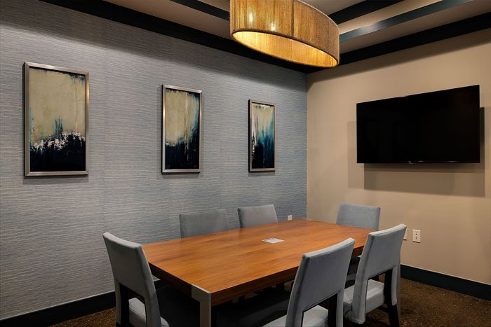 Elegant conference room featuring a sleek wooden table, modern blue chairs, abstract artwork, and a large wall-mounted TV.