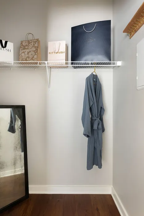 Elegant walk-in closet with a cozy robe on a hanger, stylish shopping bags on a shelf, and a full-length mirror complementing the modern design.