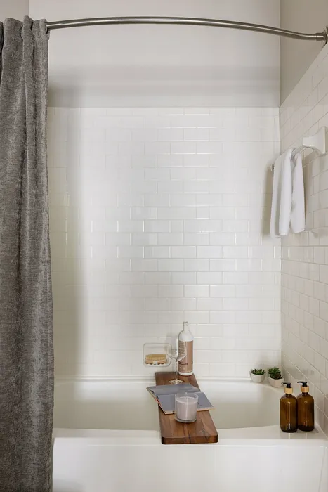 Elegant bathroom with a relaxing bathtub, stylish gray curtain, white subway tiles, and sleek bathroom accessories for a serene spa-like experience.