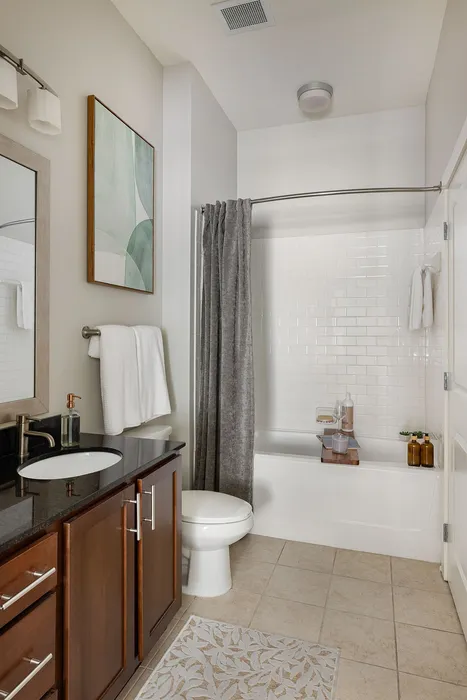 Modern bathroom featuring sleek black countertop, elegant wooden cabinetry, and a stylishly tiled bathtub with neutral tones.