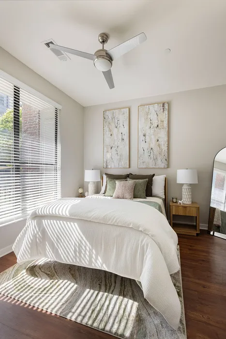 Inviting bedroom with modern ceiling fan, textured wall art, and soft natural light filtering through blinds.