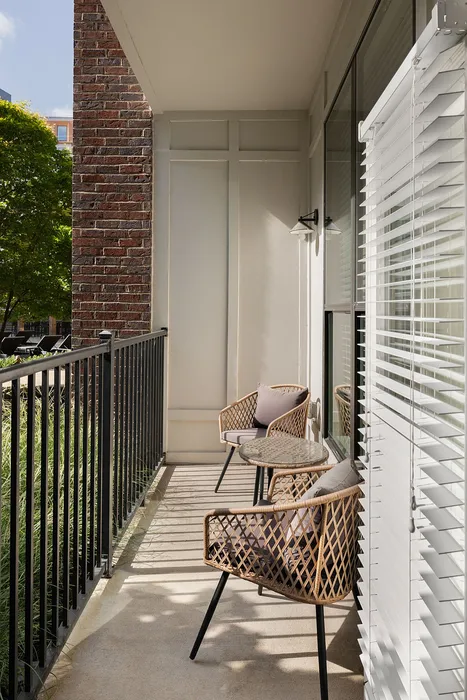 Charming balcony with stylish wicker chairs and table, bathed in soft sunlight, offering a peaceful retreat and a view of the lush greenery.