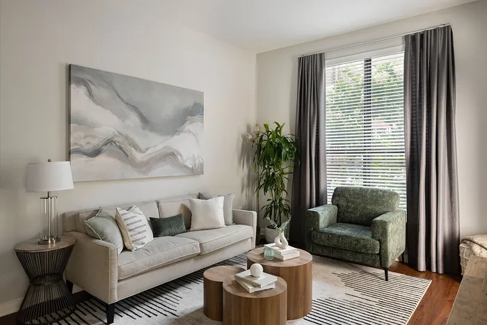 Inviting living room with elegant decor, featuring a cozy beige sofa, stylish abstract artwork, and a chic green armchair by a sunlit window. Perfect blend of comfort and style.