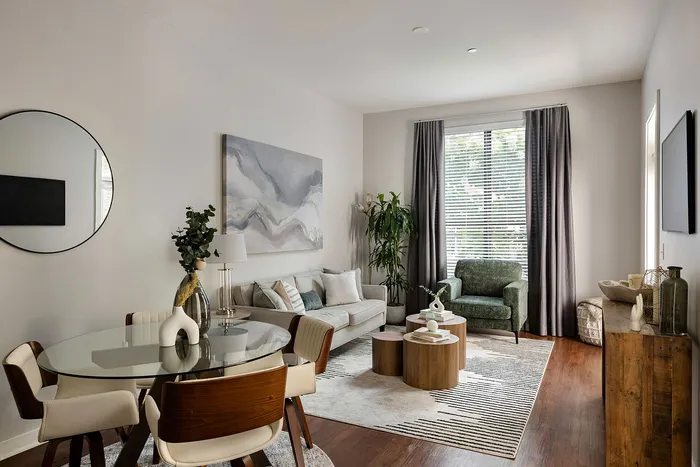 Elegant living room with modern decor, featuring a plush gray sofa, stylish round glass dining table, and a statement green armchair, bathed in natural light from large windows.