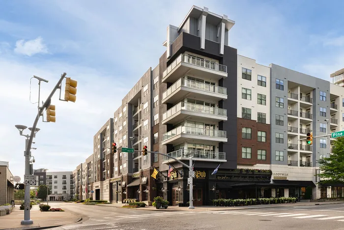 Modern urban apartment building with spacious balconies and street-level shops, located in a vibrant city corner.