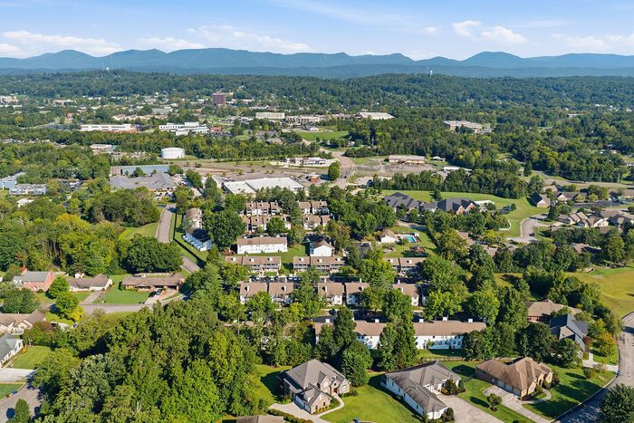 Scenic aerial view of a lush, green residential area surrounded by picturesque mountains and abundant greenery, offering tranquil living.