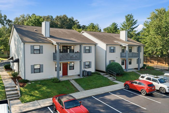 Charming two-story apartment complex with spacious balconies, nestled in a serene green setting with ample parking space.