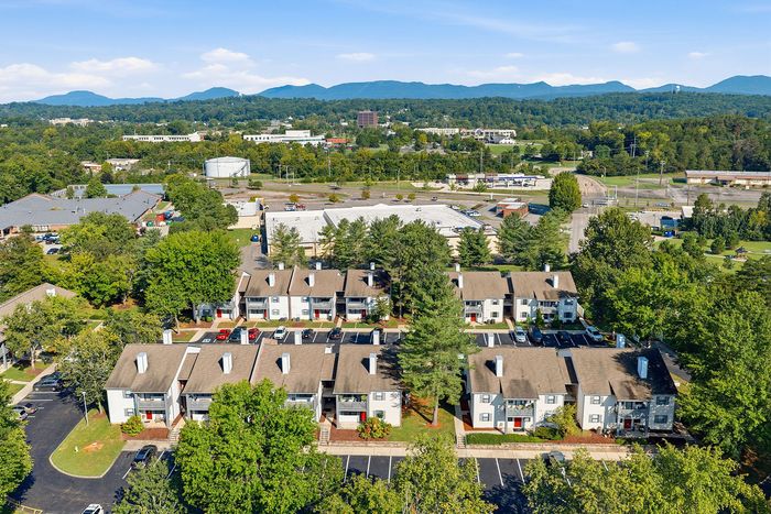 Aerial view of charming townhouse community nestled in lush greenery with a backdrop of scenic mountains, highlighting attractive homes and spacious parking areas.